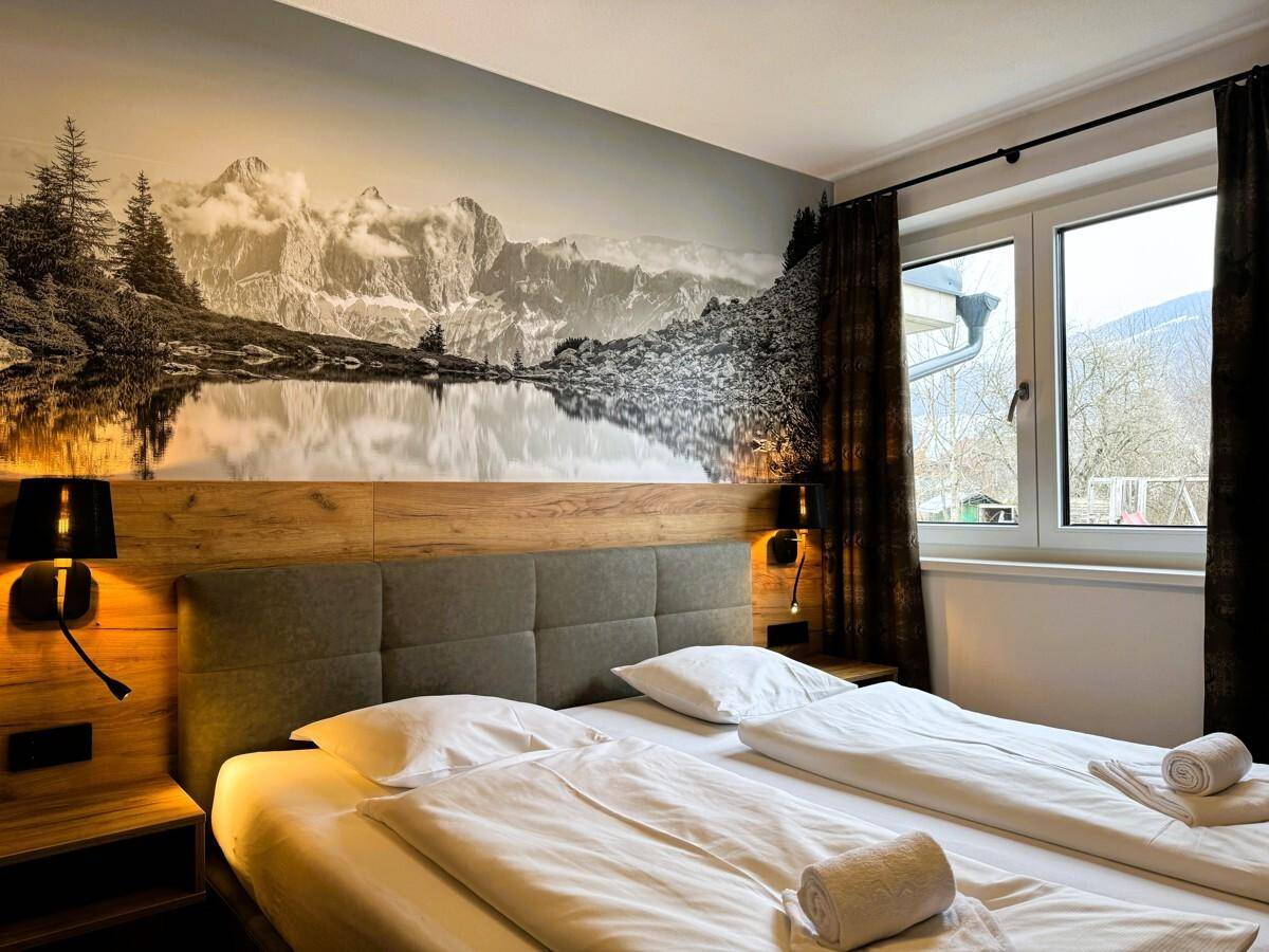 Schlafzimmer mit Doppelbett, Holzkopfteil und großer Wandtapete mit Bergmotiv.