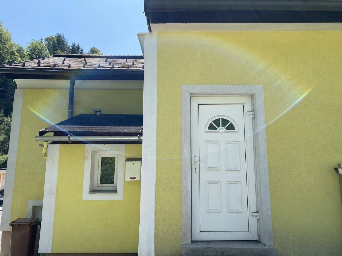Weißer Eingangsbereich mit Haustür und gelber Fassade des Gebäudes, sonnig und klar.