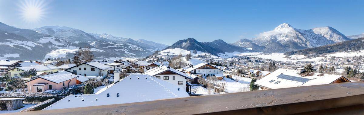 Weitläufiger Panoramablick vom Balkon über die verschneite Berglandschaft und das Dorf.