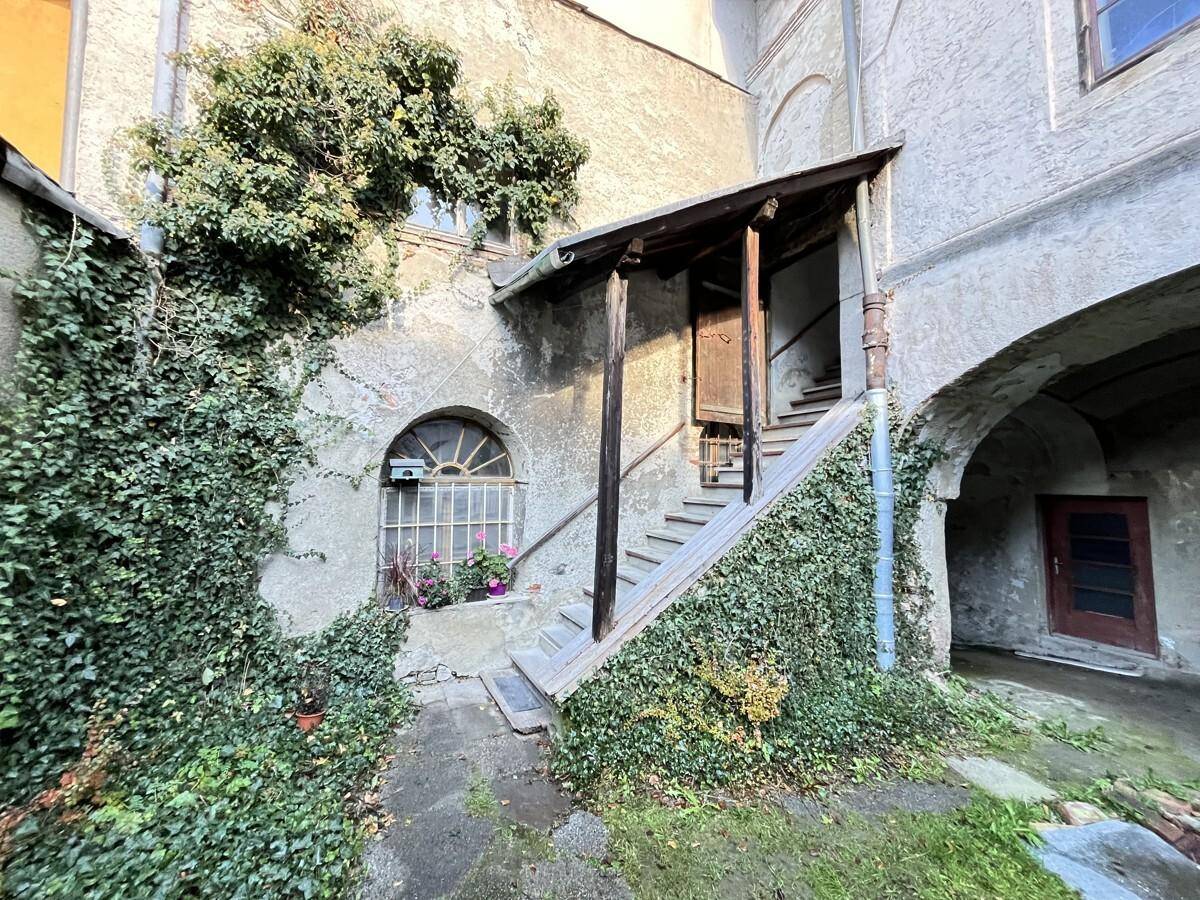 Alte Fassade eines Gebäudes mit Efeu bewachsen, einer Außentreppe und einem Rundbogenfenster.
