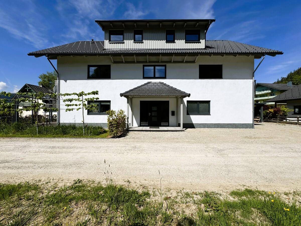 Vorderansicht eines modernen Gebäudes mit weißer Fassade und großem Vorplatz.