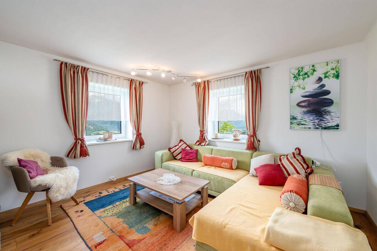 Helles Wohnzimmer mit bequemer Eckcouch, Holztisch und farbenfrohen Vorhängen.