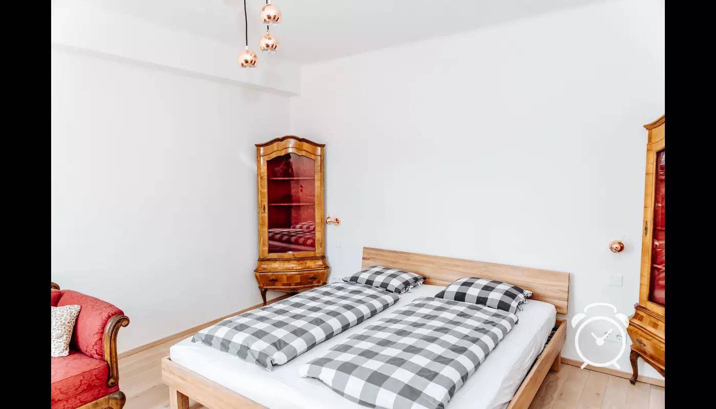 Schlafzimmer mit Doppelbett, antikem Vitrinenschrank und rotem Sofa.