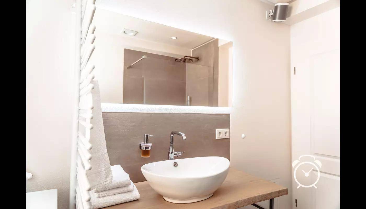 Modernes Badezimmer mit ovalem Waschbecken, großem Spiegel und Handtuchheizkörper.