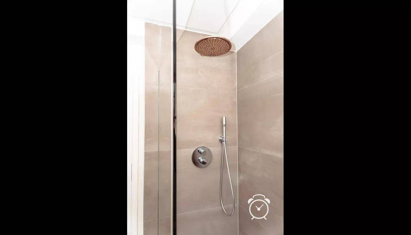 Moderne Dusche mit Regenduschkopf und beigefarbenen Fliesen.