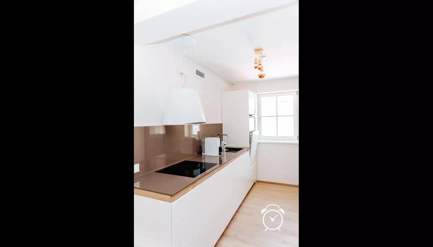 Moderne Einbauküche mit weißen Fronten, Induktionskochfeld und Holzarbeitsplatte.