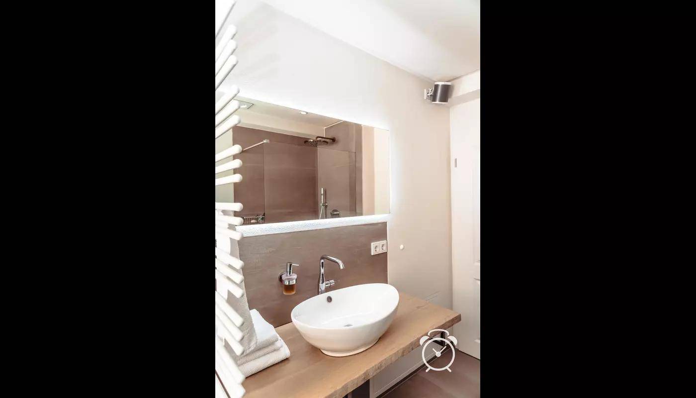 Modernes Badezimmer mit ovalem Waschbecken auf Holzplatte und großem Spiegel.