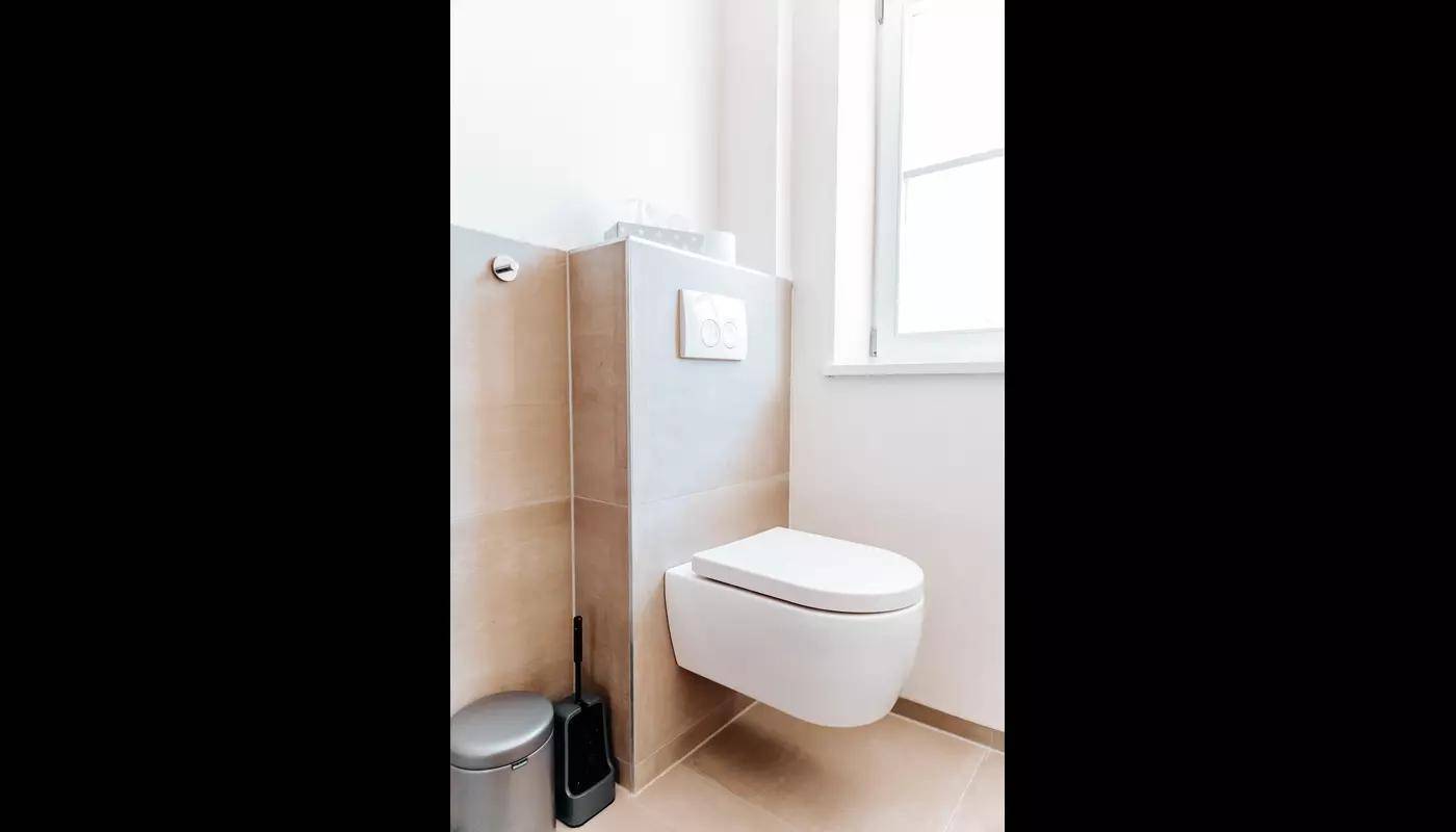 Modernes WC mit wandhängender Toilette und beigefarbenen Fliesen.