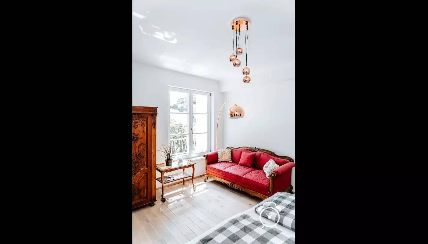 Helles Schlafzimmer mit rotem Sofa, Holzboden und modernen Hängelampen.