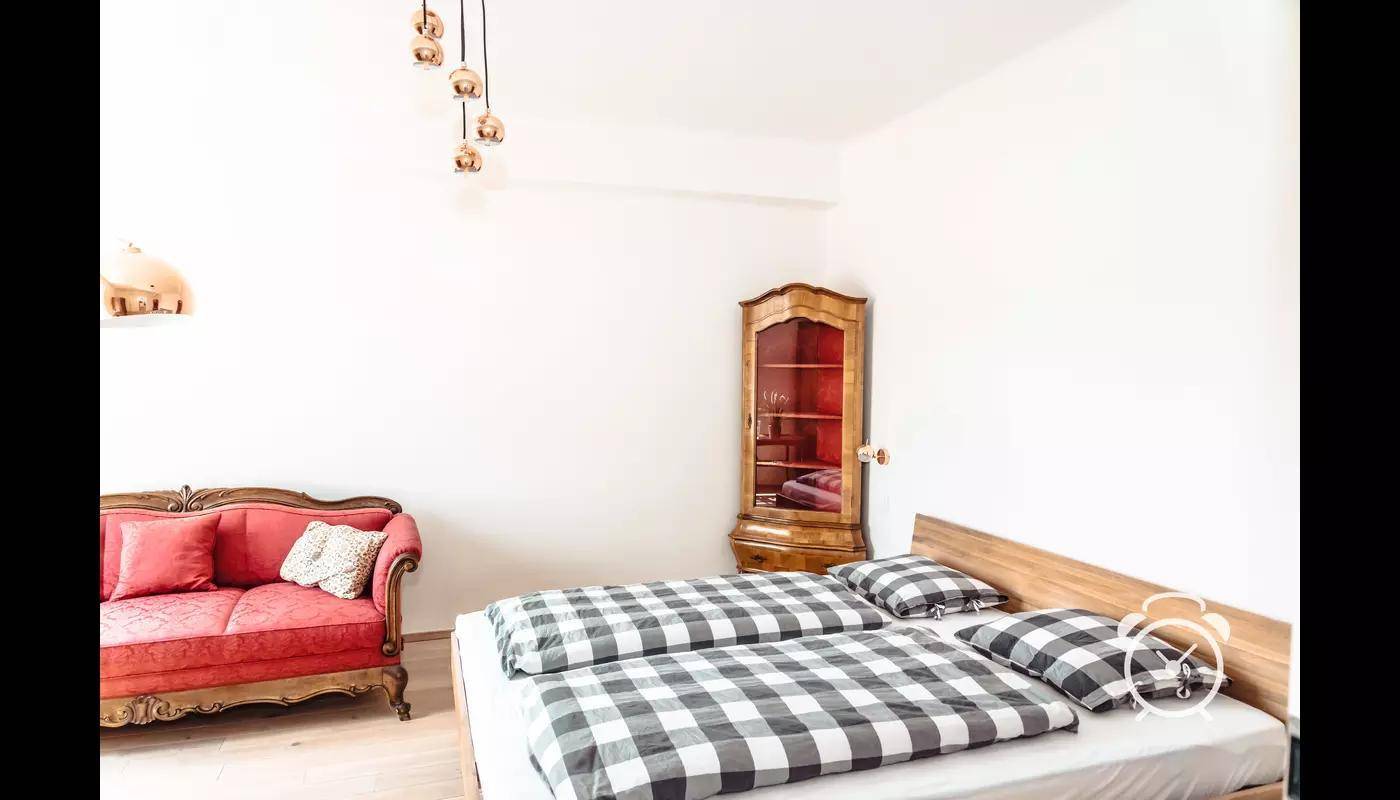 Schlafzimmer mit Doppelbett, rotem Sofa und antikem Vitrinenschrank.