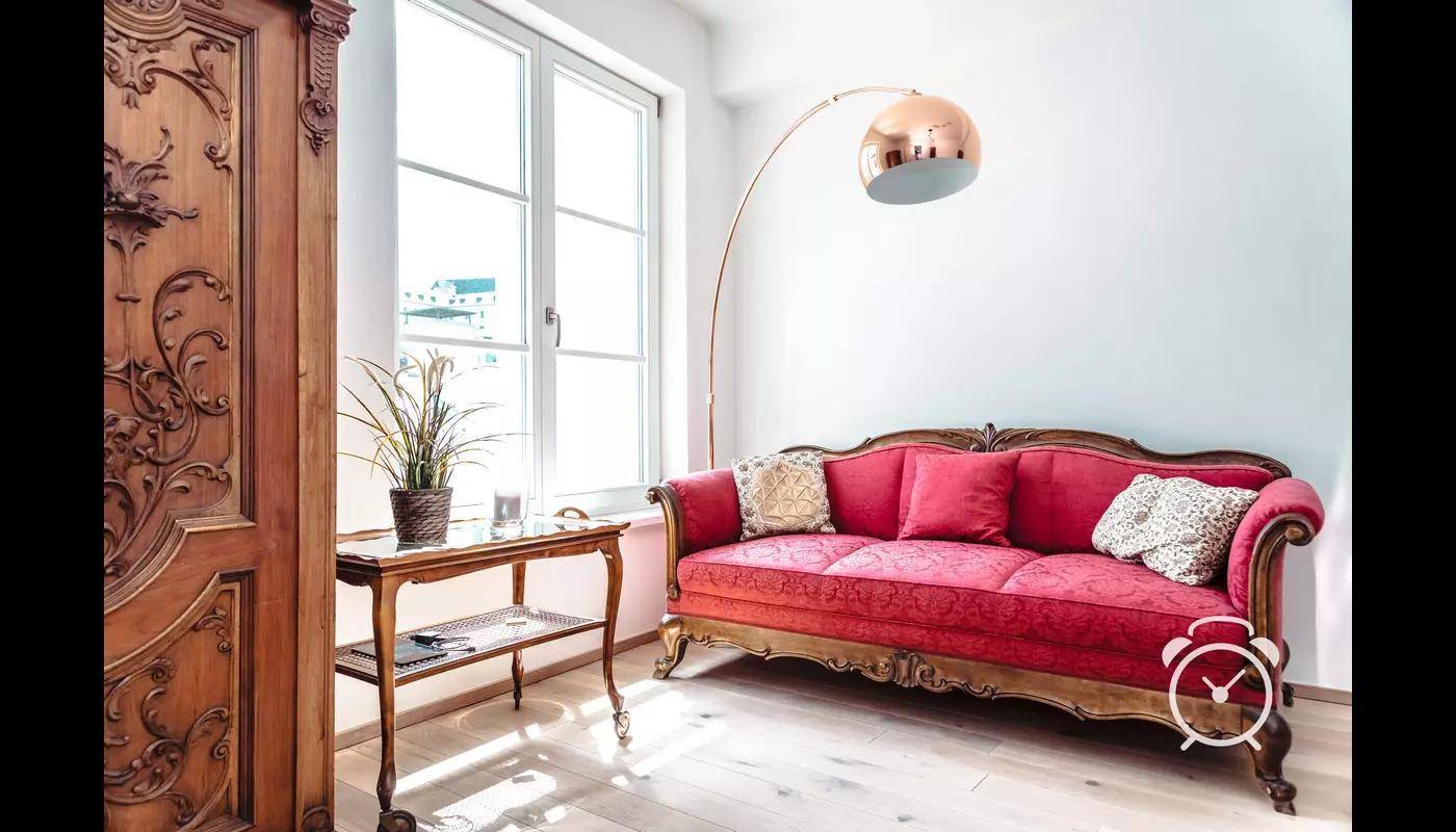 Gemütliches Schlafzimmer mit rotem Sofa, Beistelltisch und großem Fenster.