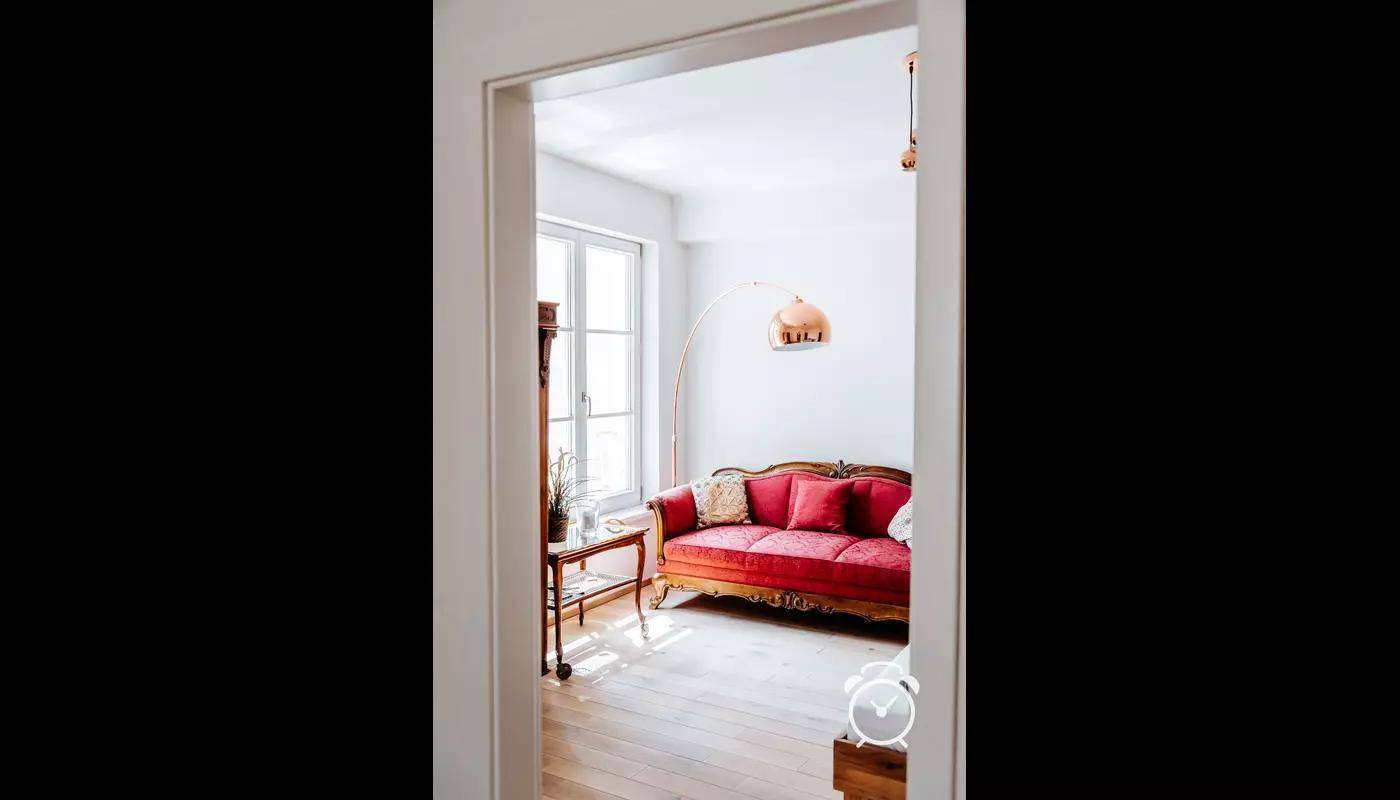 Blick in ein helles Schlafzimmer mit rotem Sofa und großem Fenster.