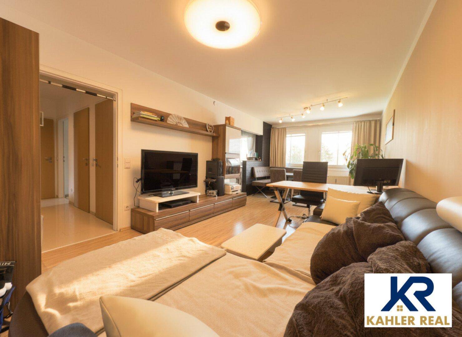 Gemütlicher Wohnbereich mit Sofa, Fernseher und integriertem Arbeitsplatz am Fenster.