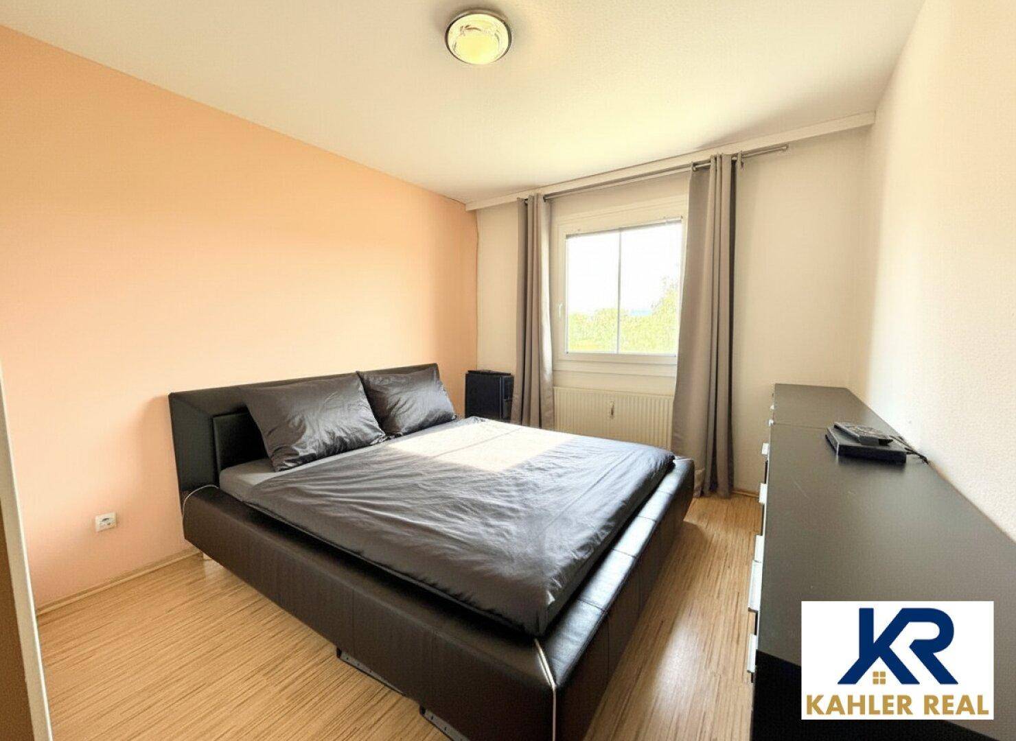 Schlafzimmer mit Doppelbett, Laminatboden und großem Fenster für viel Tageslicht.