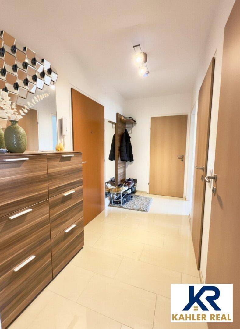 Heller Eingangsbereich mit Fliesenboden, Garderobe und praktischer Kommode mit Spiegel.