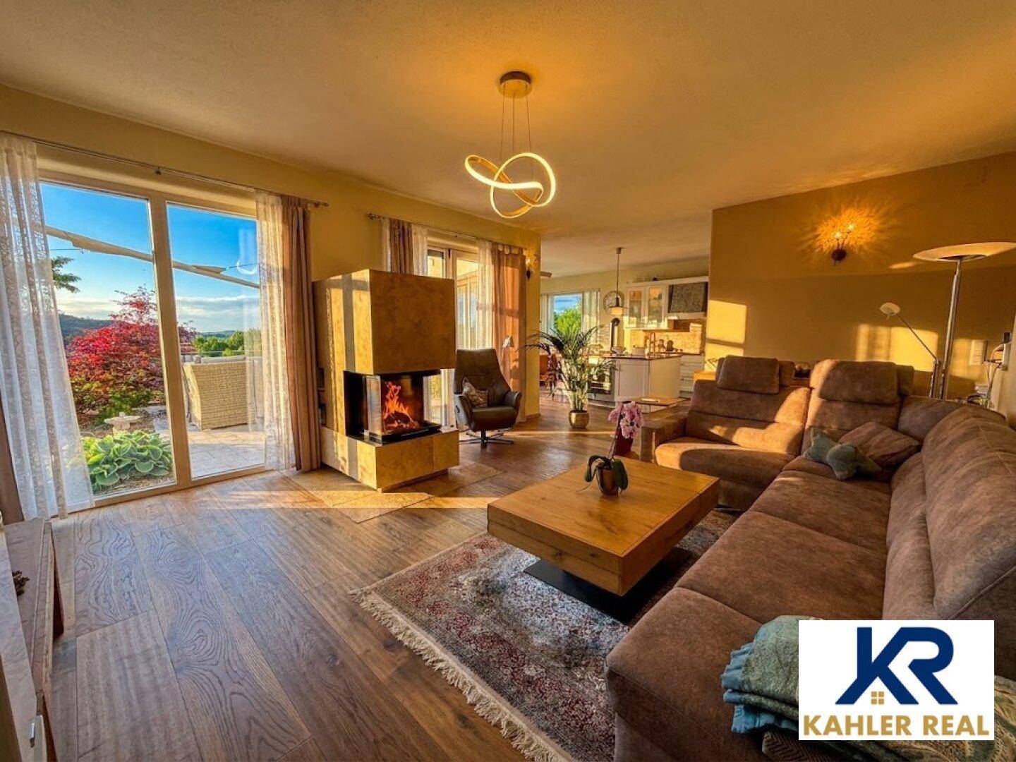Helles Wohnzimmer mit Kamin, Holzboden und Zugang zur Terrasse mit weitem Ausblick.