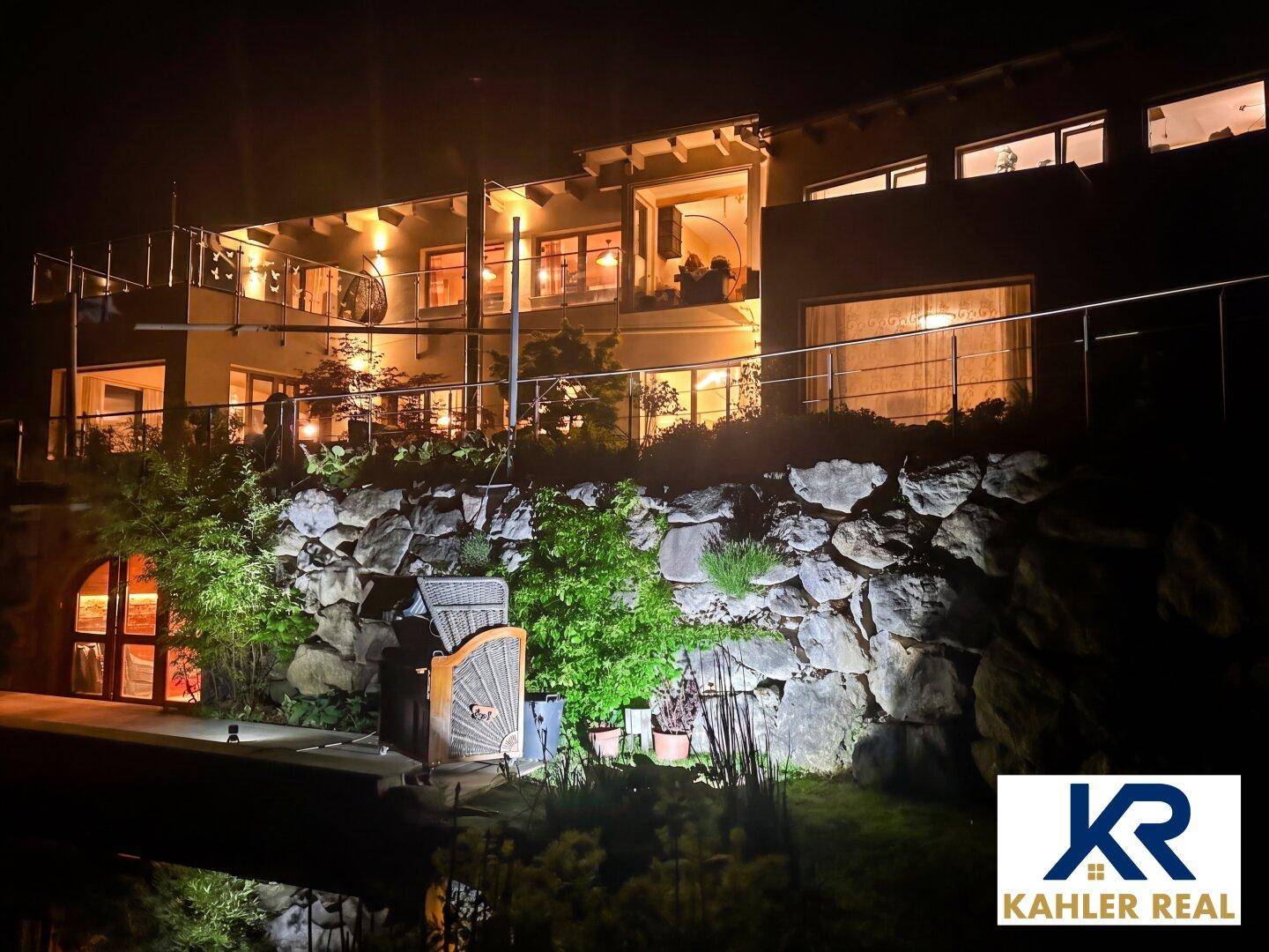 Beleuchtetes Anwesen bei Nacht mit stimmungsvoller Gartenbeleuchtung und Teich.