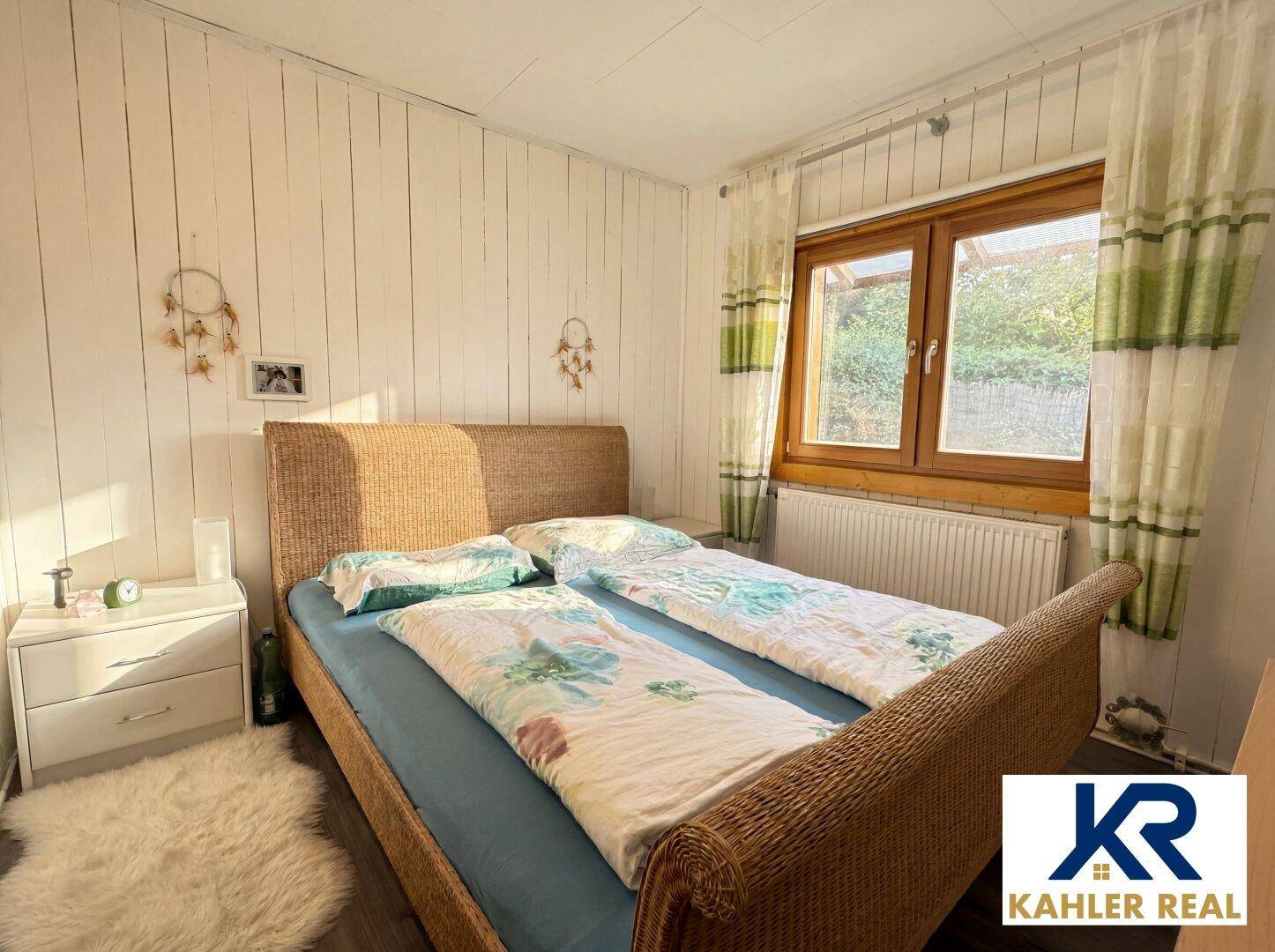 Gemütliches Schlafzimmer mit Holzwänden, Rattanbett und Fenster mit Blick ins Grüne.
