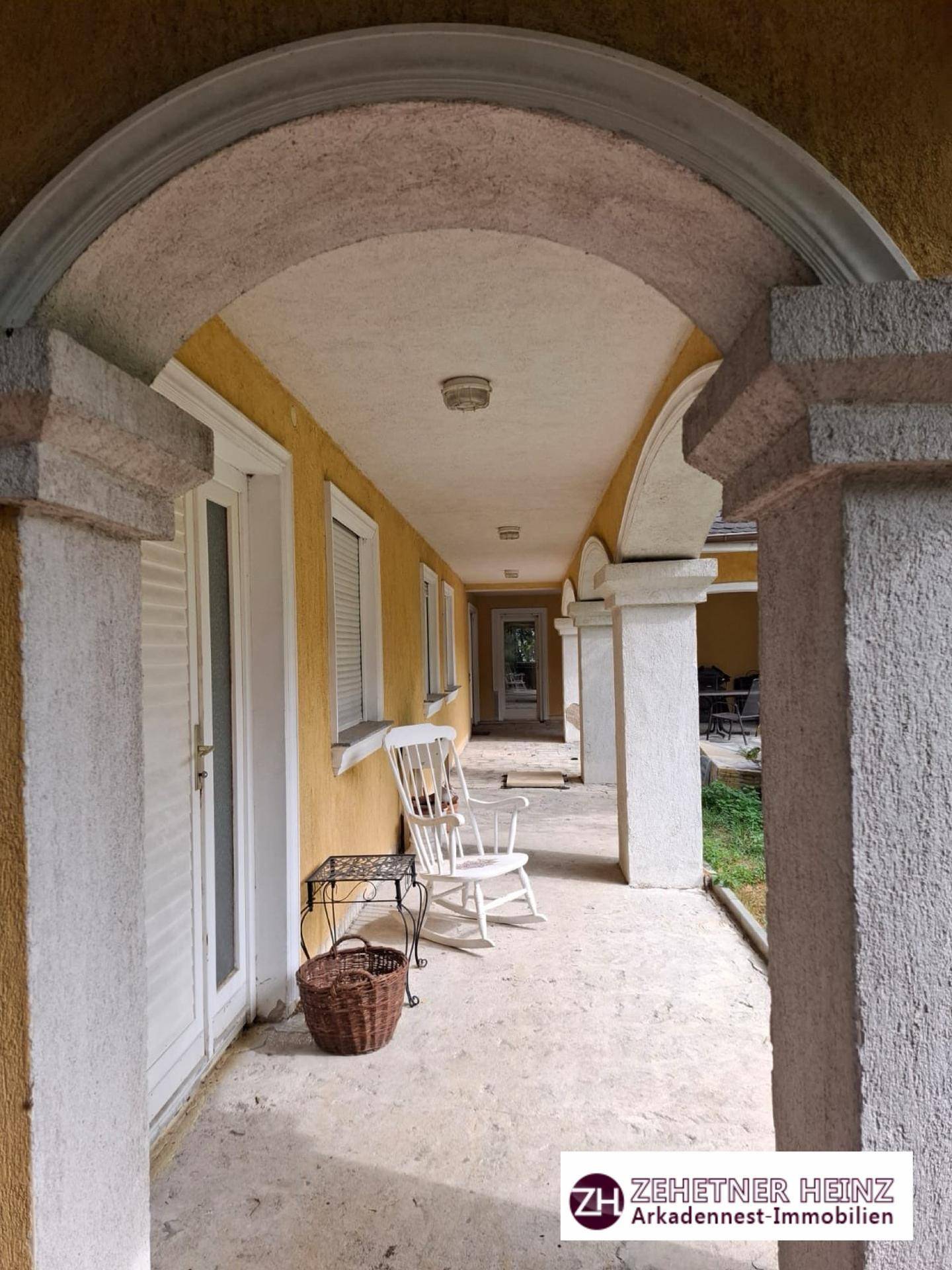 Lange überdachte Loggia entlang der Hausfassade mit Säulen und Blick ins Grüne.