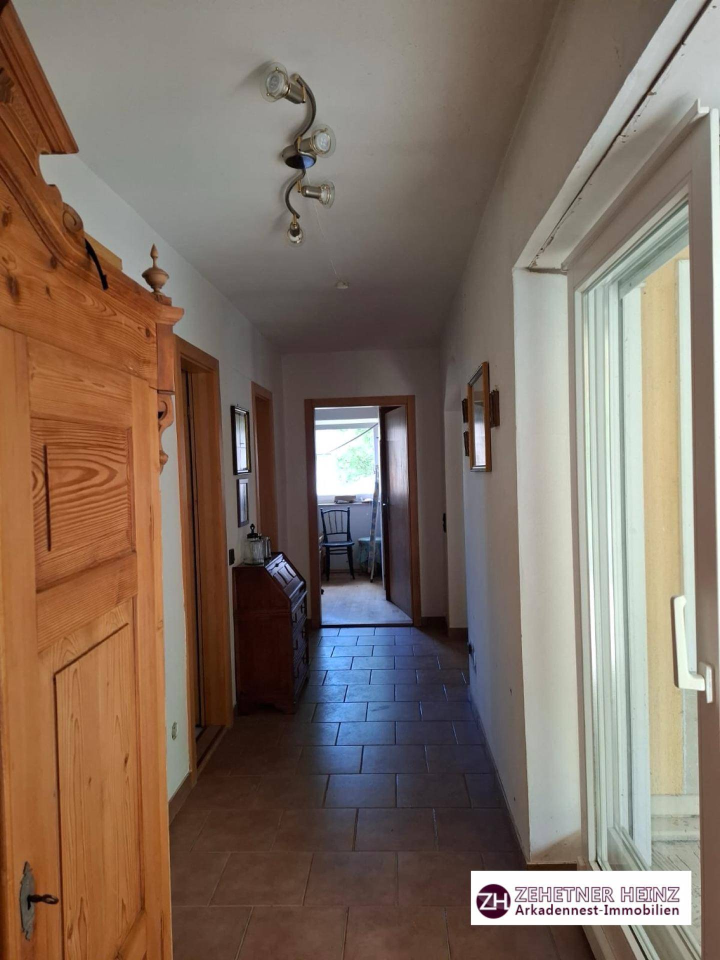 Flur mit Terrakottafliesen, Holzschrank und Zugang zu weiteren Räumen.
