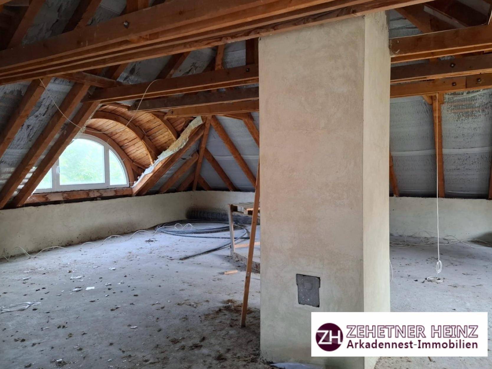 Unausgebauter Dachboden mit sichtbaren Holzbalken und Gaubenfenster.