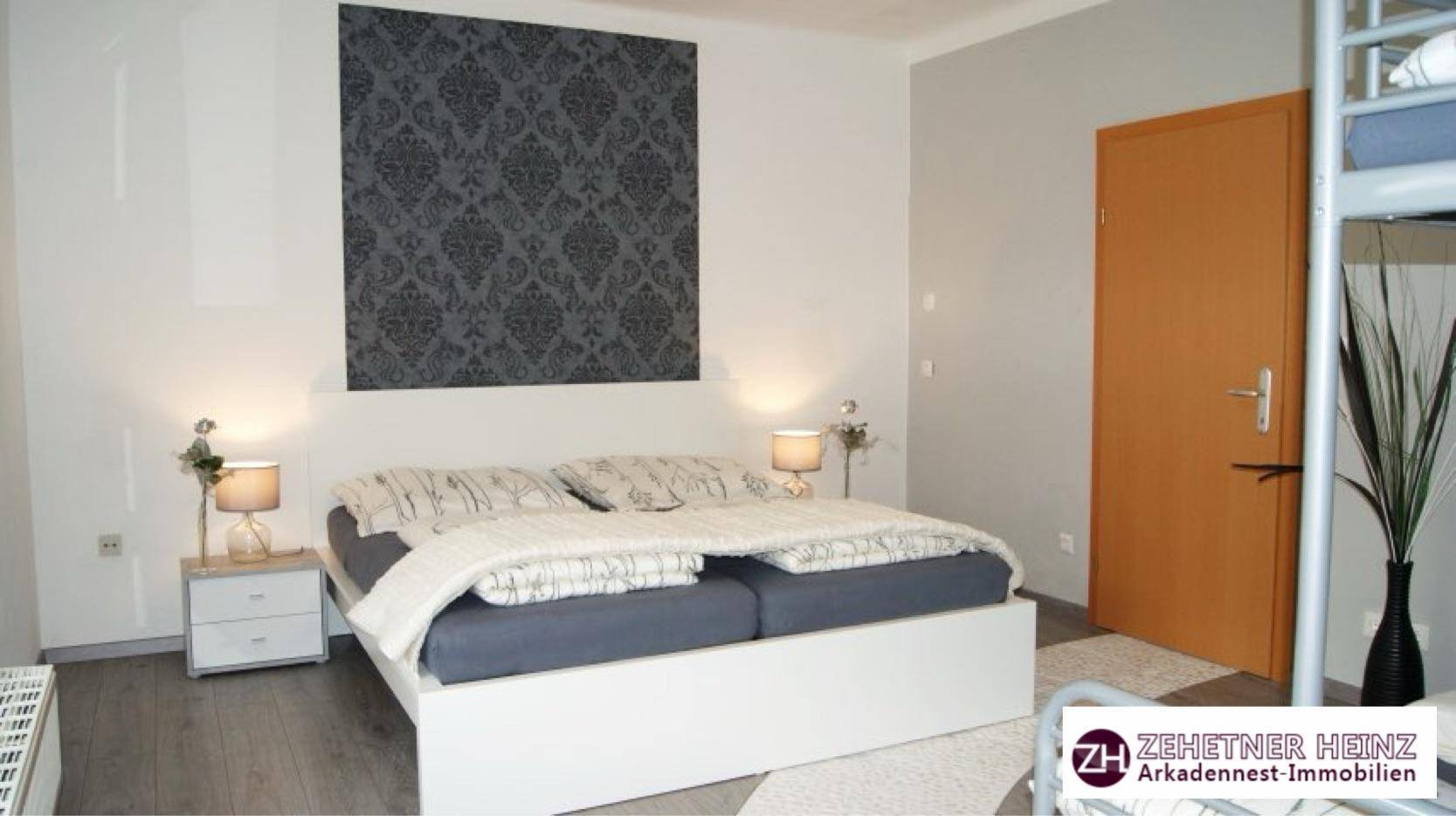 Schlafzimmer mit Doppelbett, modernem Akzentwand und dunklem Holzfußboden.