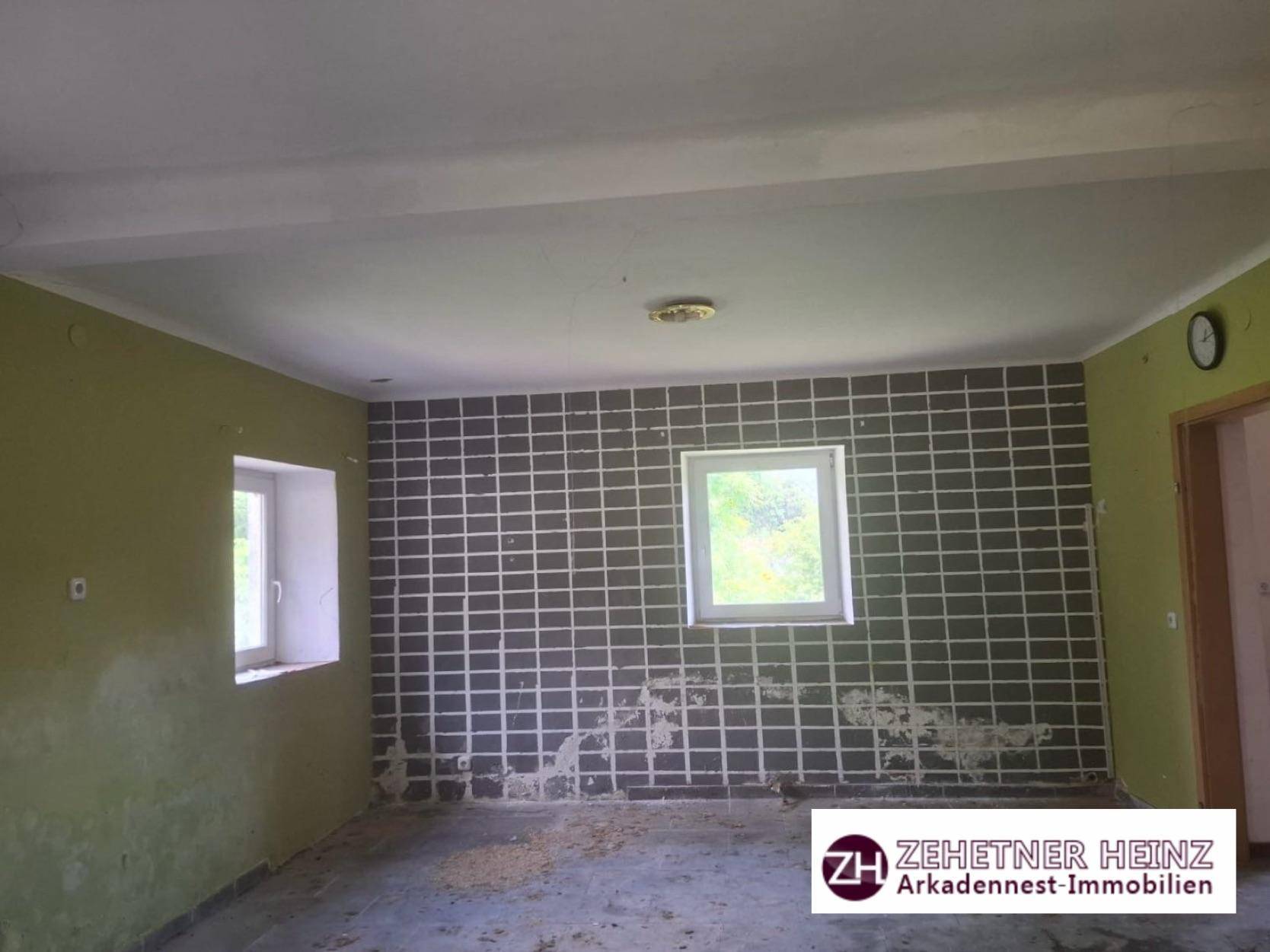 Raum mit teilweise gefliesten Wänden in Dunkelgrau und grünen Wänden, mit einem Fenster.