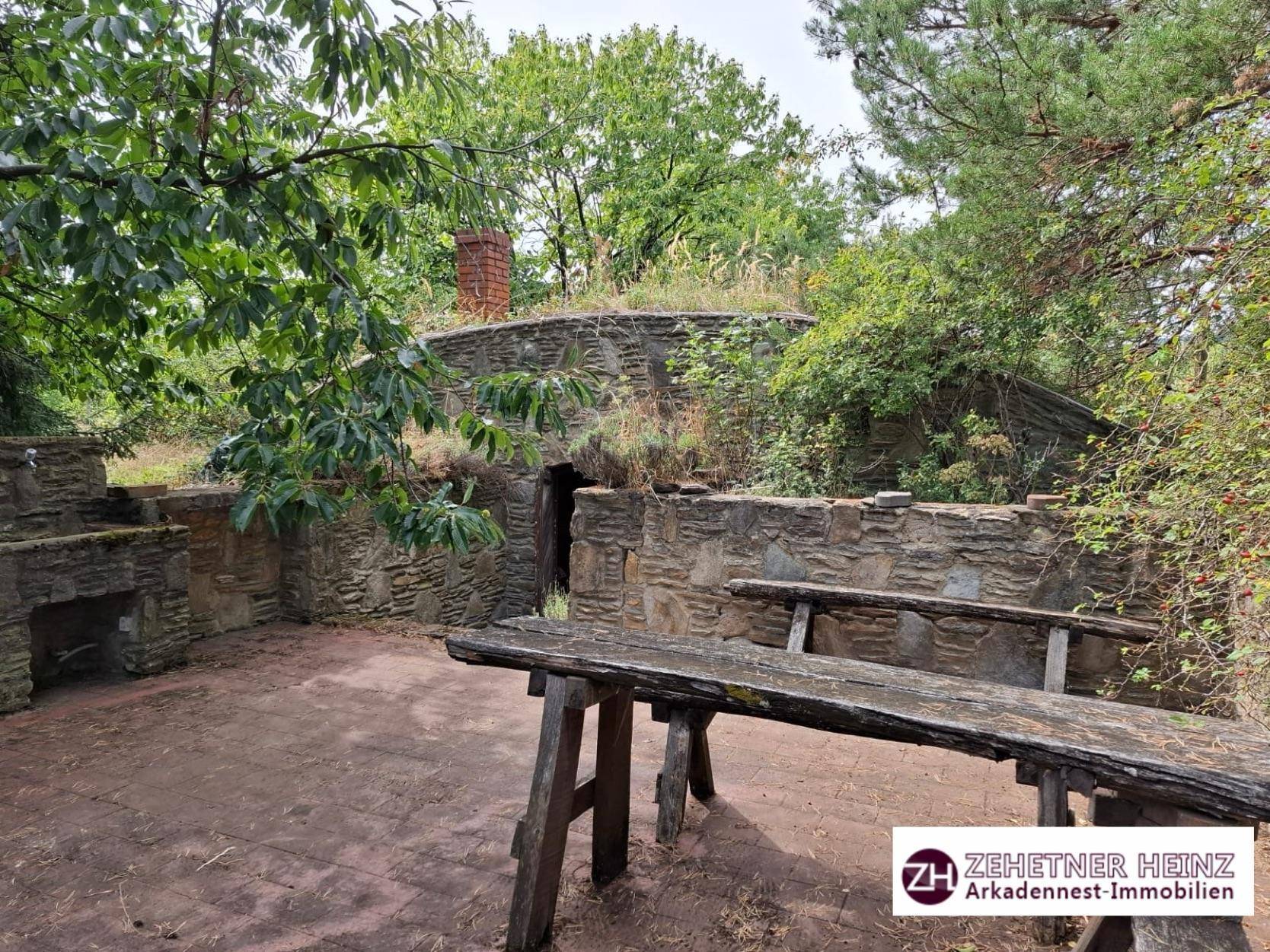 Gepflasterter Außenbereich mit Holzbänken und einem traditionellen Erdkeller mit Grasdach.