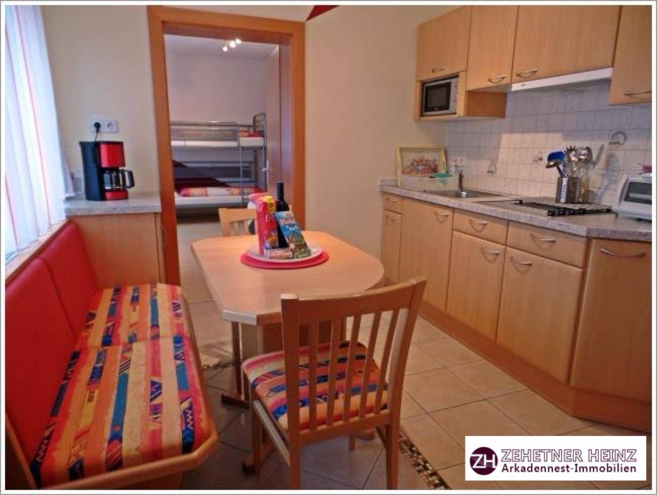 Gemütliche Wohnküche mit Holzeinbauten, Essecke und Blick in ein angrenzendes Schlafzimmer.