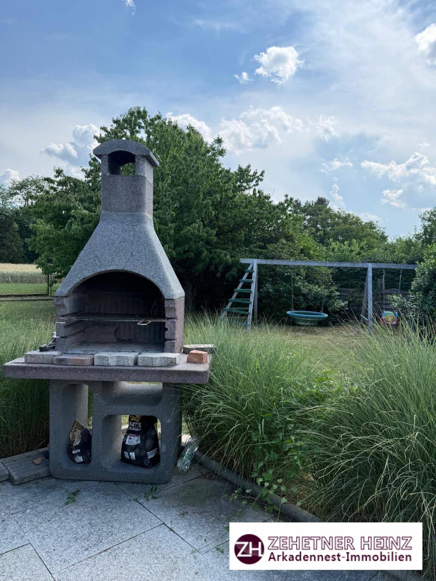 Gemütlicher Grillplatz im Garten mit Steingrill und einem Spielplatz im Hintergrund.