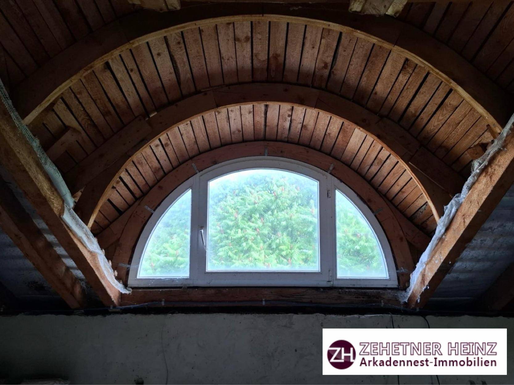 Rundes Gaubenfenster im Dachboden mit Blick auf die Baumwipfel.
