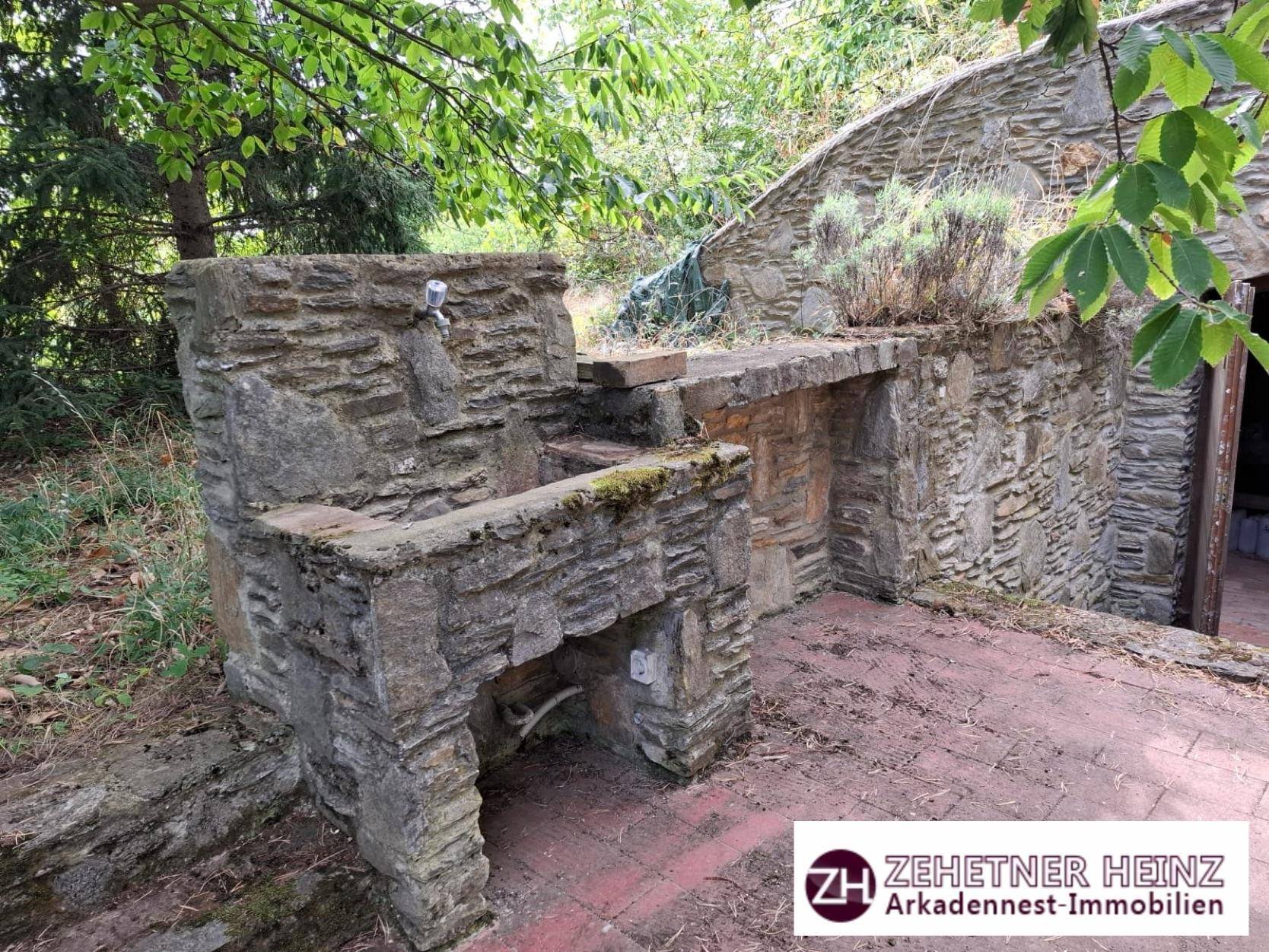 Steinerne Außenküche oder Grillplatz mit Wasserhahn und Arbeitsfläche im Freien.