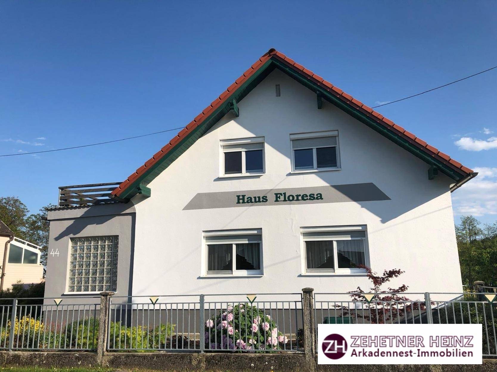 Vorderansicht des Hauses mit weißer Fassade, Satteldach und einem blühenden Rosenbusch im Vorgarten.