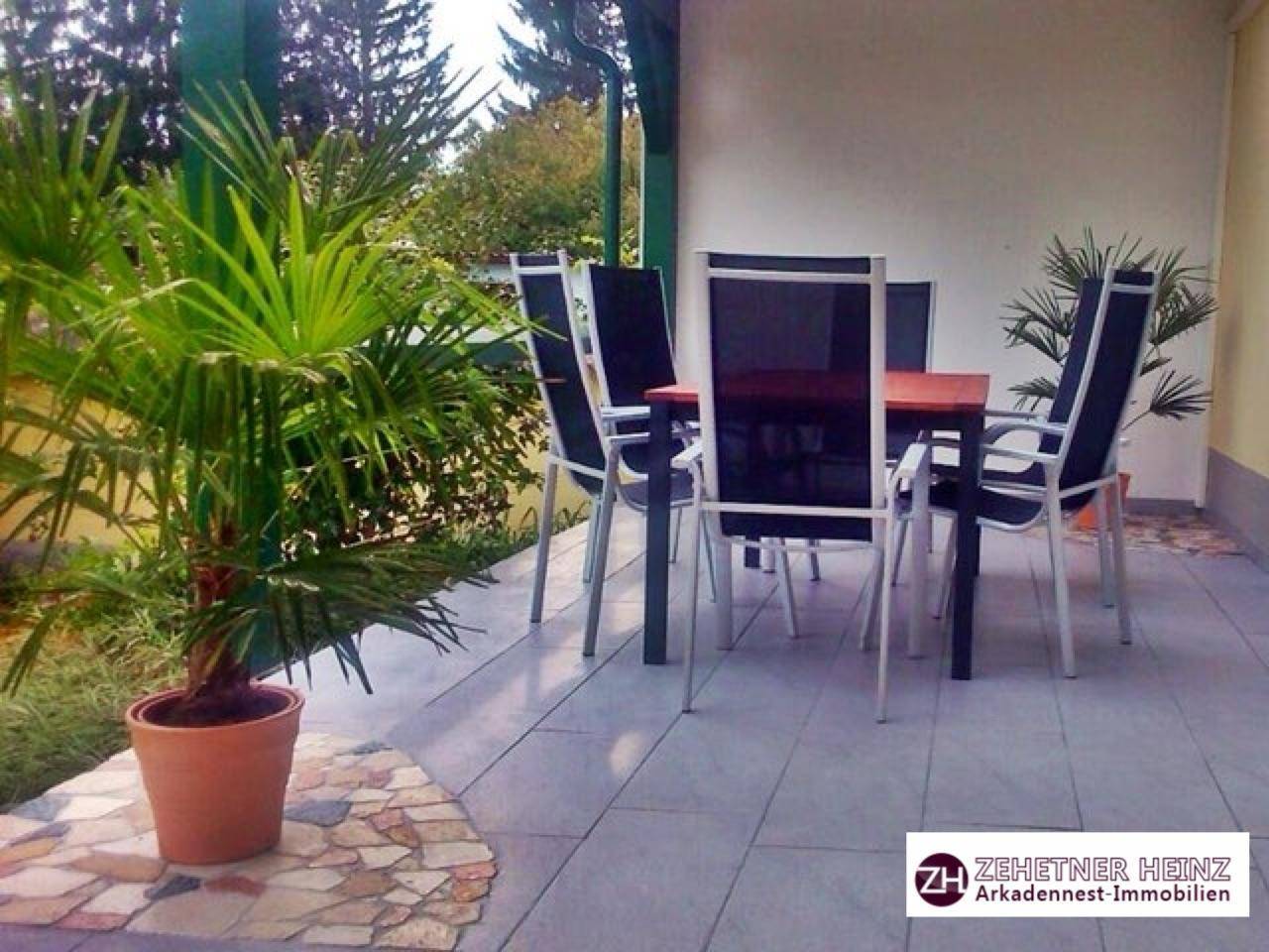 Überdachte Terrasse mit Fliesenboden, Esstisch und Stühlen, umgeben von Topfpflanzen.