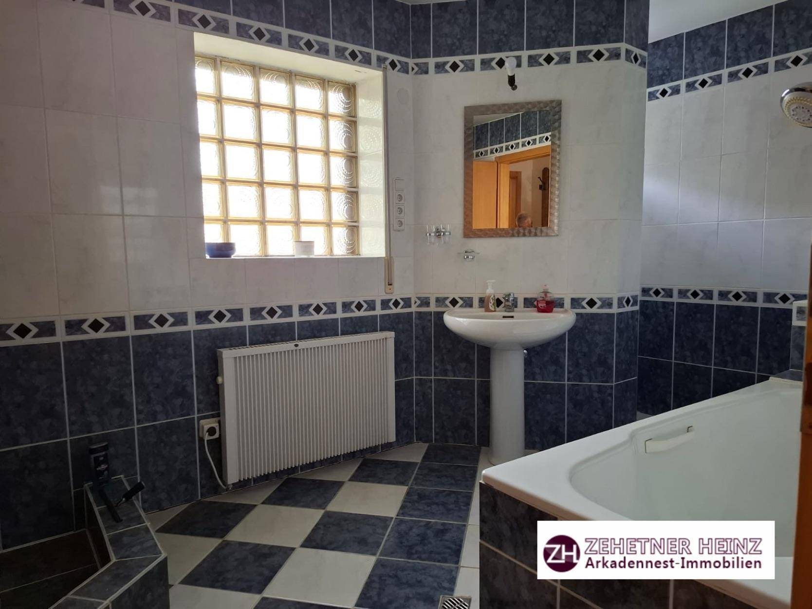 Badezimmer mit blauen und weißen Fliesen, Badewanne und Duschbereich.