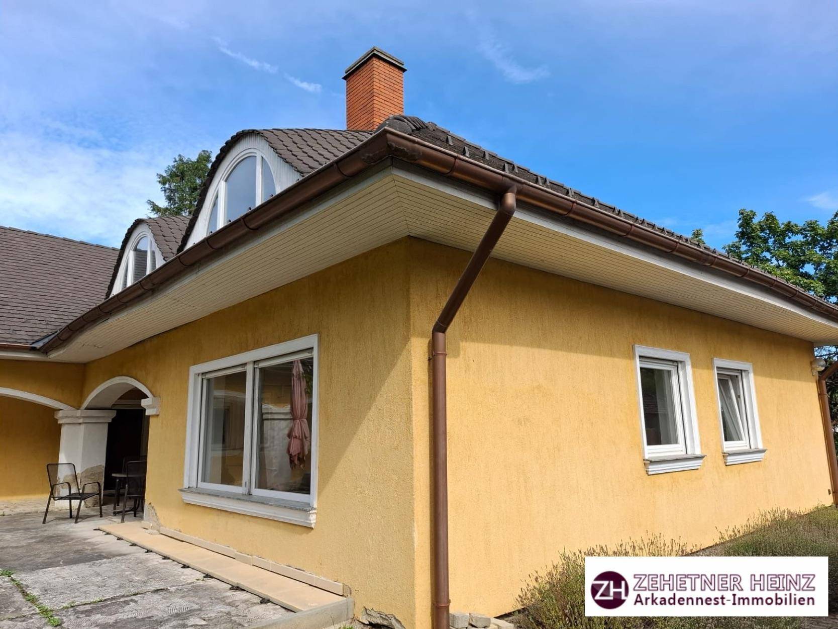 Seitenansicht des Hauses mit gelber Fassade, Regenrinne und Fenstern.