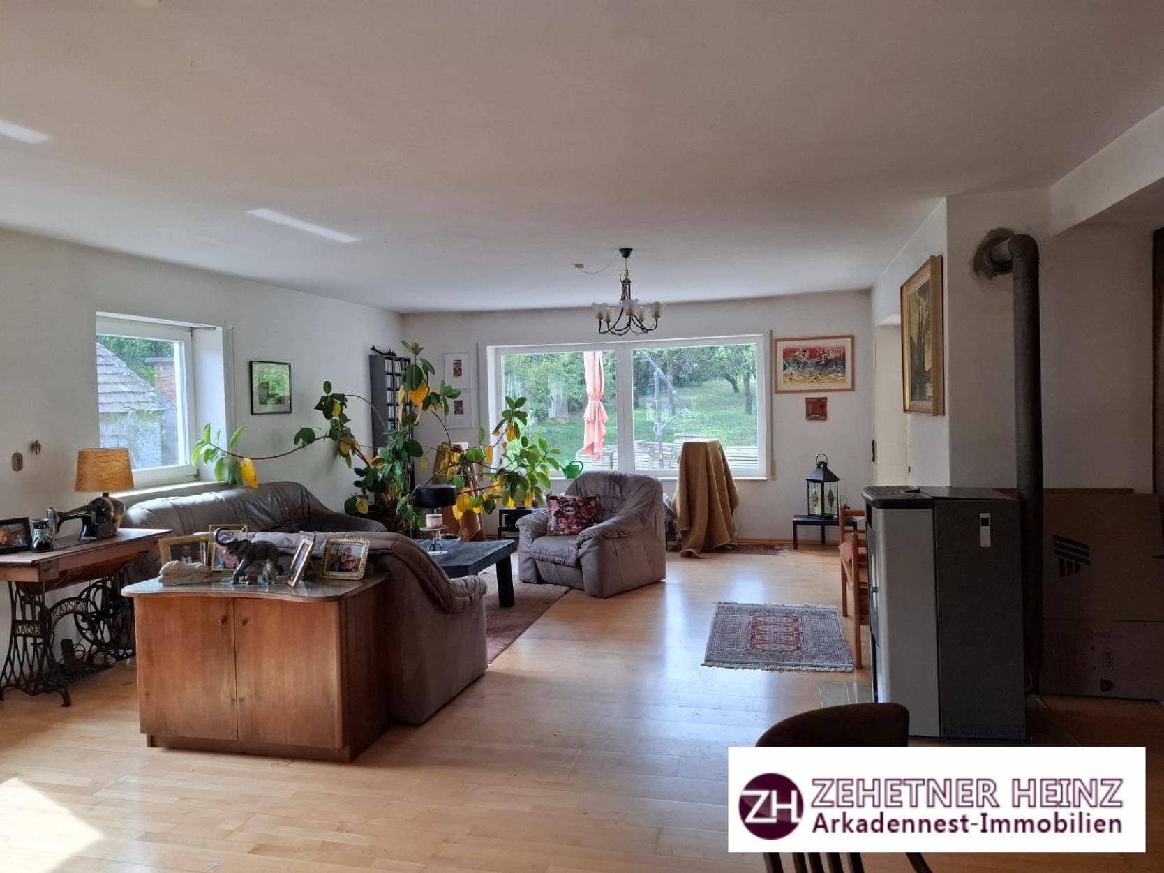 Geräumiges Wohnzimmer mit hellem Parkettboden, vielen Pflanzen und Kaminofen.