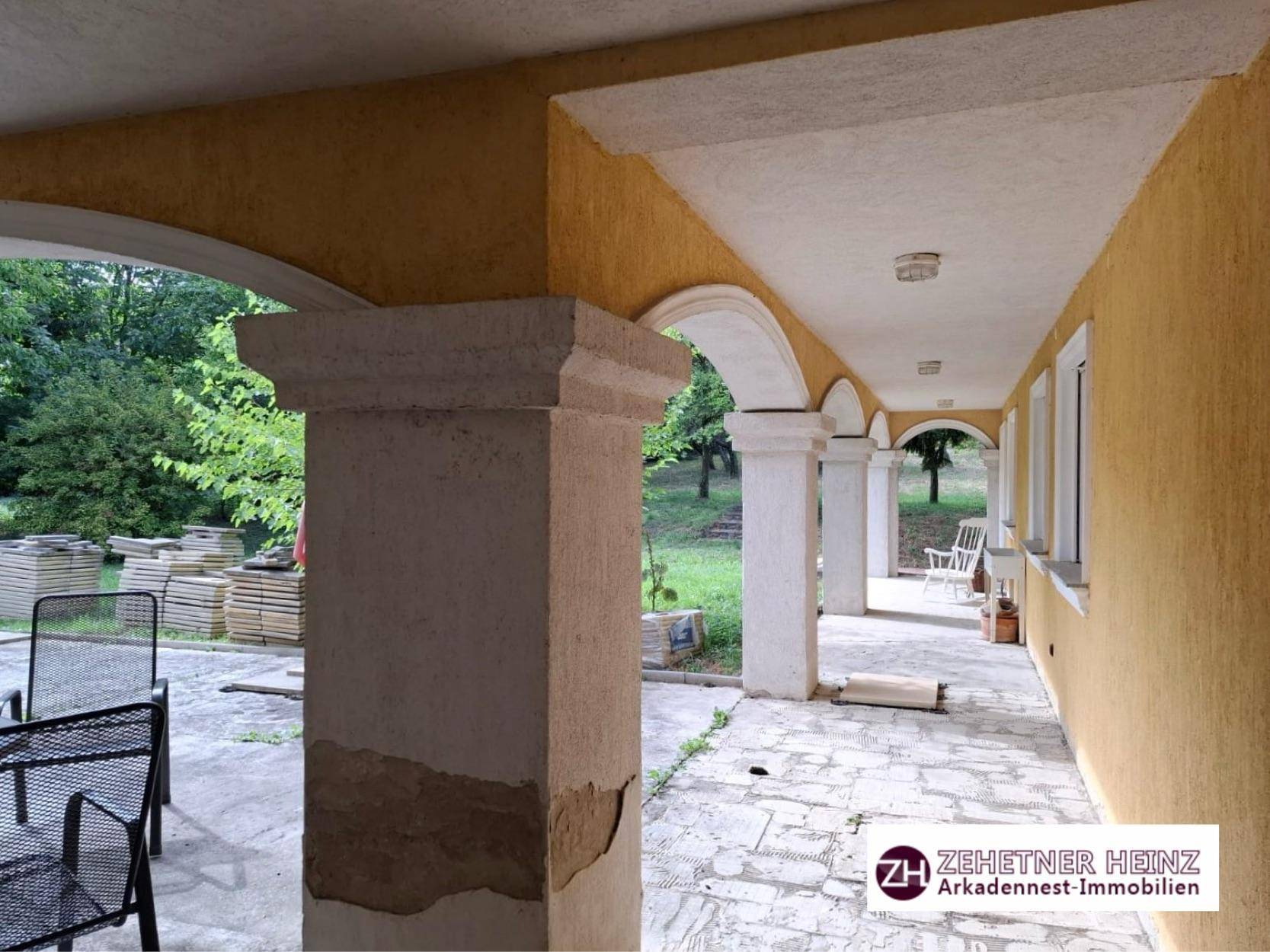 Lange überdachte Loggia mit Säulen und Sitzgelegenheiten, die zum Garten führt.