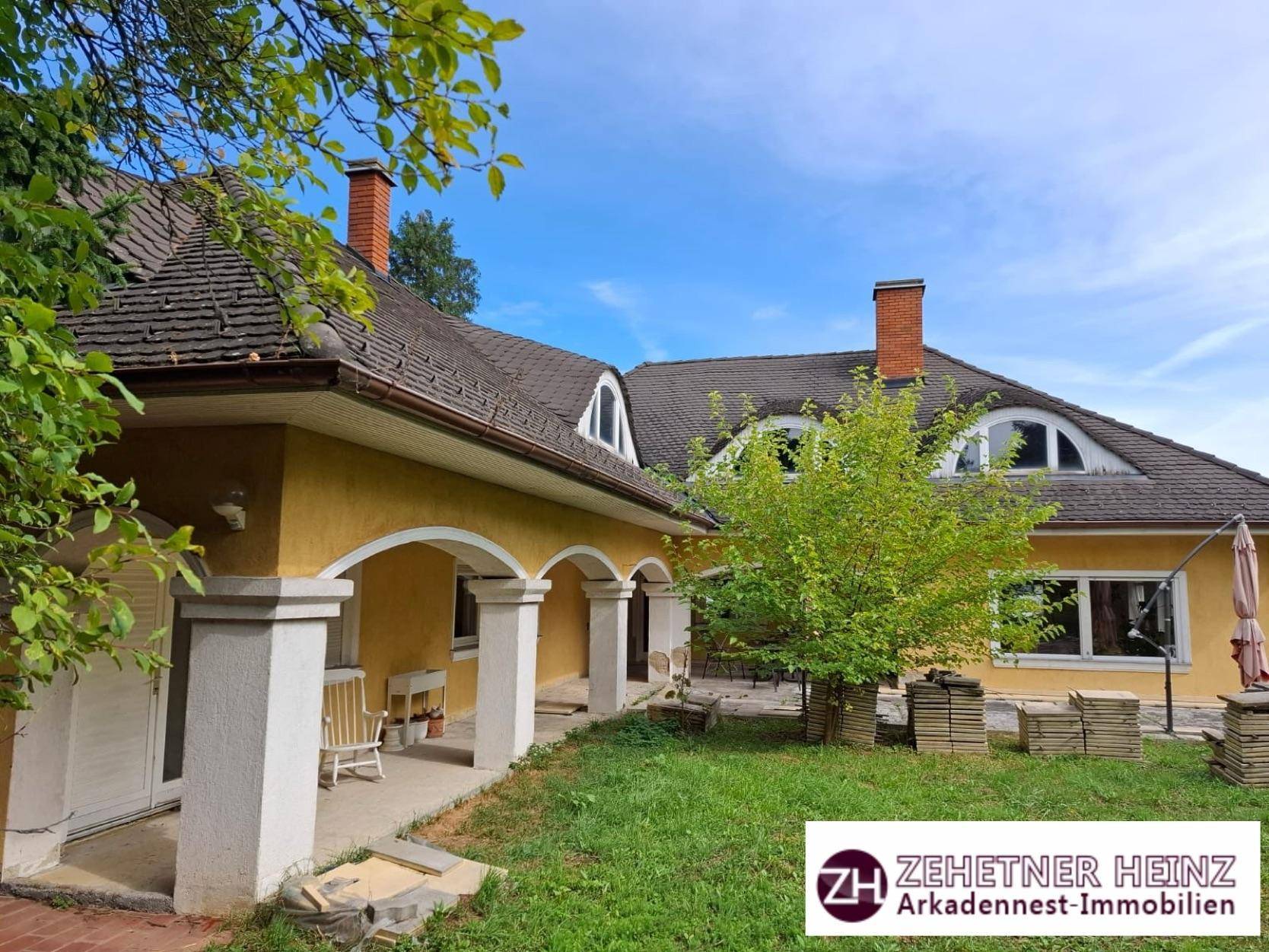 Gelbes Haus mit Satteldach, Gaubenfenstern und großem Garten mit altem Baumbestand.