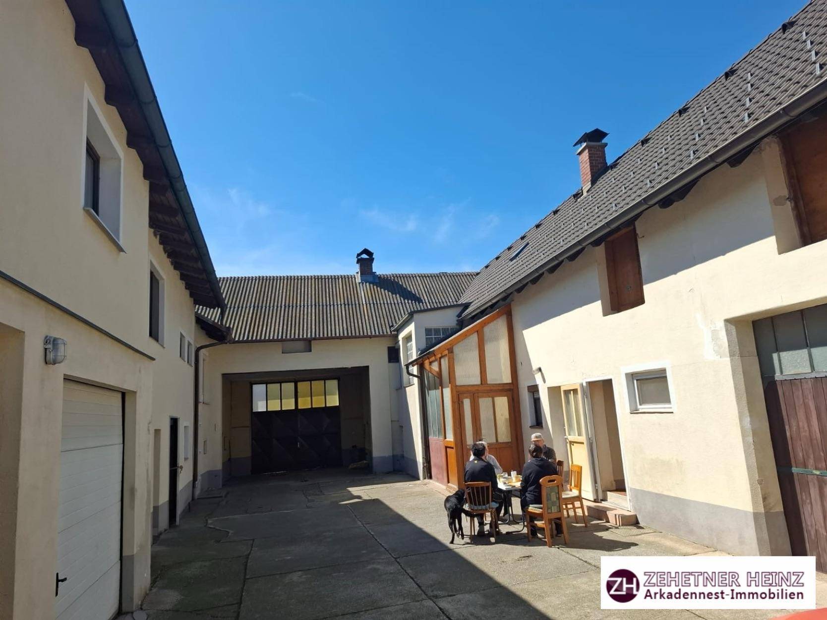 Sonniger Innenhof mit Sitzgelegenheiten und mehreren Gebäuden im ländlichen Stil.