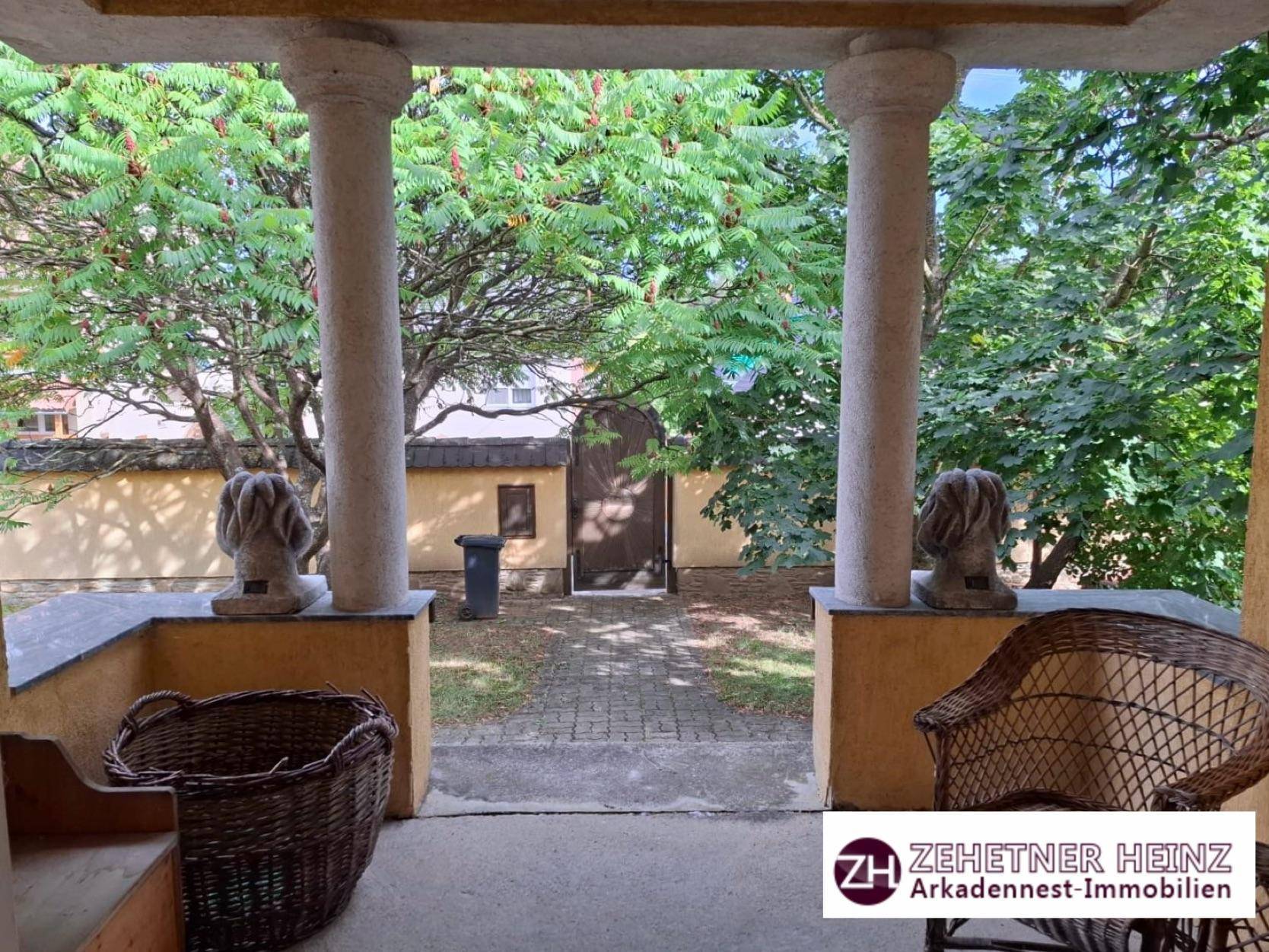 Überdachte Loggia mit Säulen und Blick auf den gepflasterten Eingangsbereich und Garten.