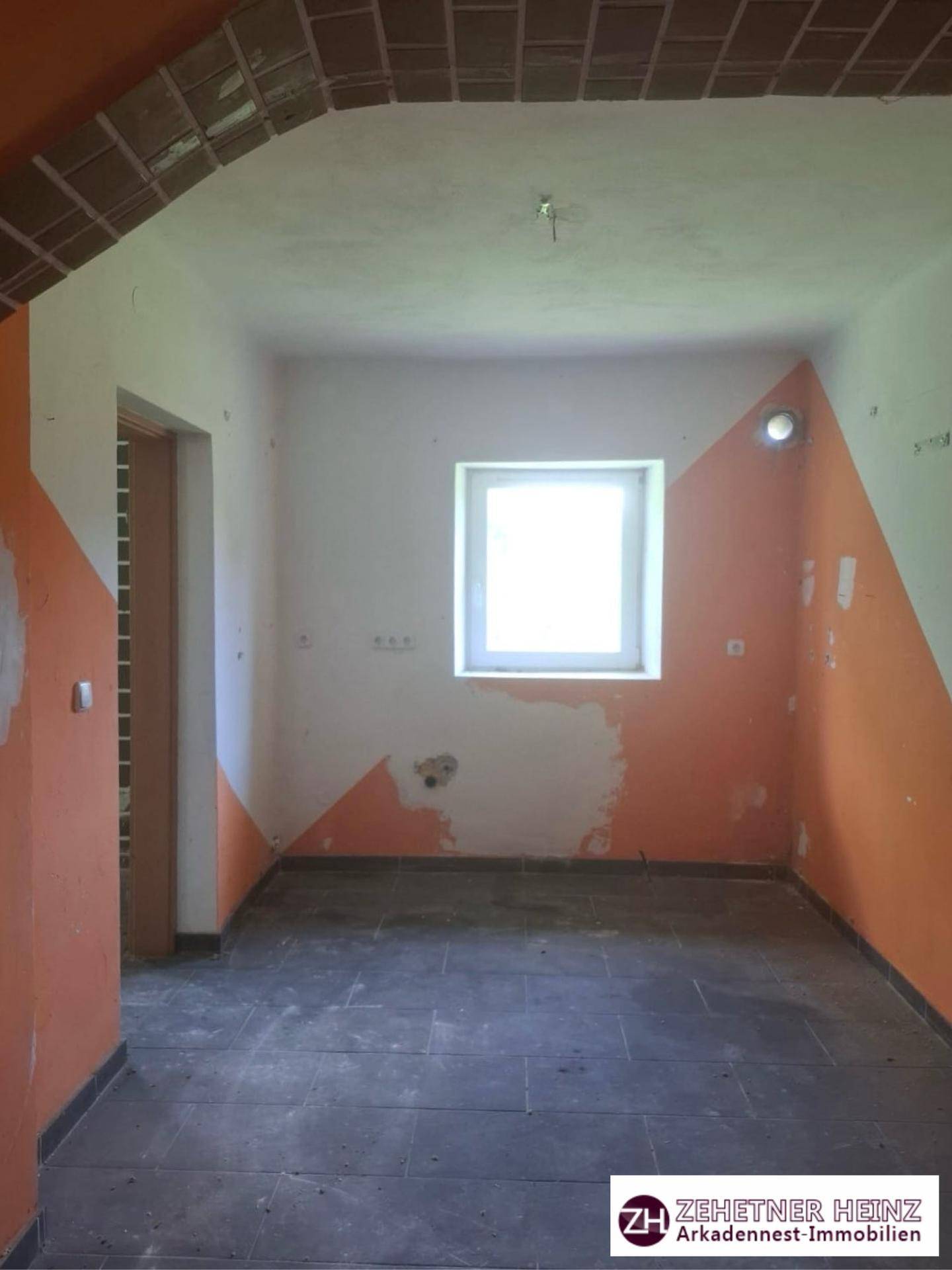 Leerer Raum mit orange-weißen Wänden, einem Fenster und deutlichen Renovierungsbedarfen.