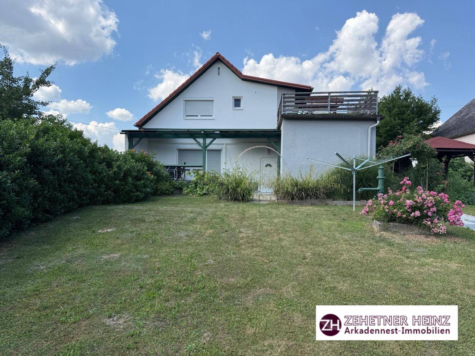 Rückansicht des Hauses mit großem Rasen, überdachter Terrasse und Wäschespinne.