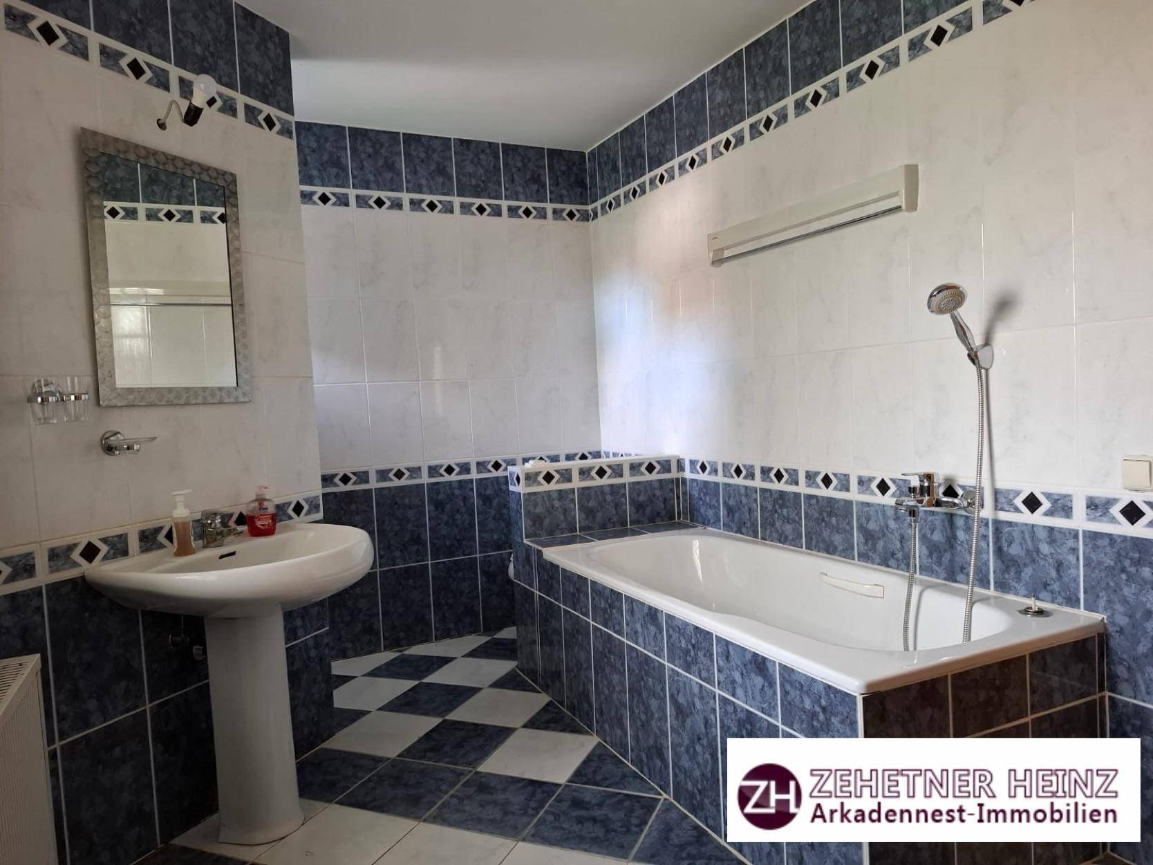 Badezimmer mit Badewanne, Waschbecken und Spiegel, gefliest in Blau und Weiß.