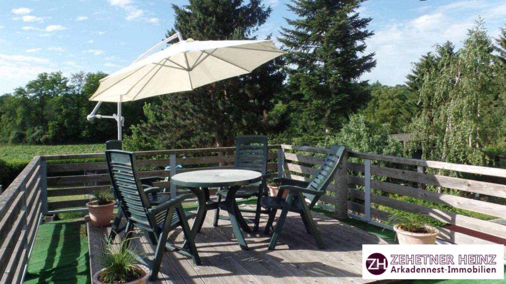 Geräumiger Holzbalkon mit Gartenmöbeln und Sonnenschirm, bietet einen weiten Blick ins Grüne.
