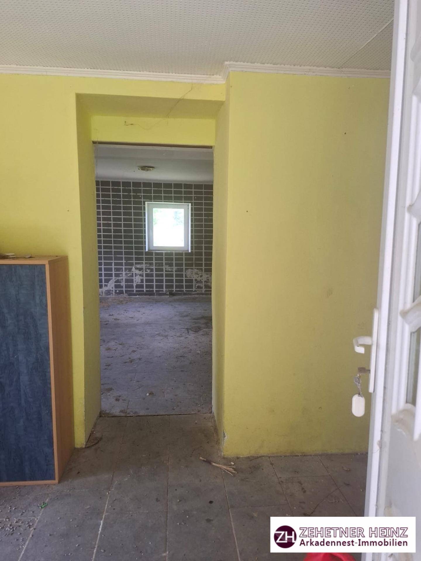 Türöffnung von einem gelb gestrichenen Raum in einen weiteren Raum mit gefliesten Wänden.