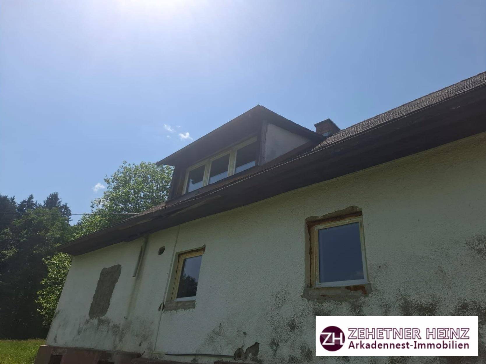 Ältere Hausfassade mit Dachgaube und deutlichen Abnutzungsspuren unter blauem Himmel.