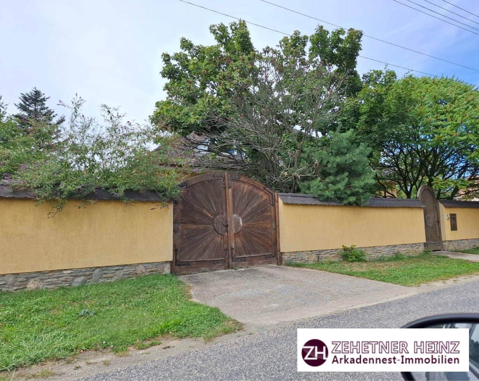 Eingang zum Grundstück mit großer Holztür und gelber Mauer zur Straße hin.