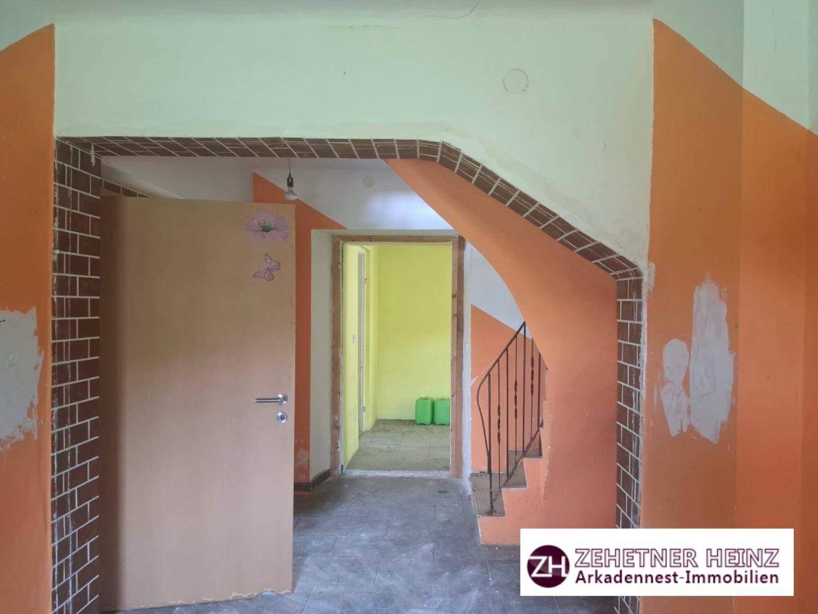 Eingangsbereich mit Treppe, teilweise orange gestrichenen Wänden und sichtbaren Renovierungsspuren.