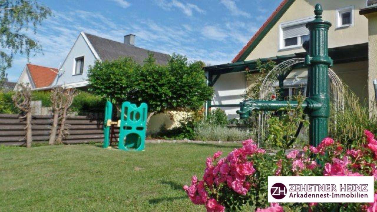 Gepflegter Garten mit Spielgerät, dekorativer Wasserpumpe und blühenden Rosen.